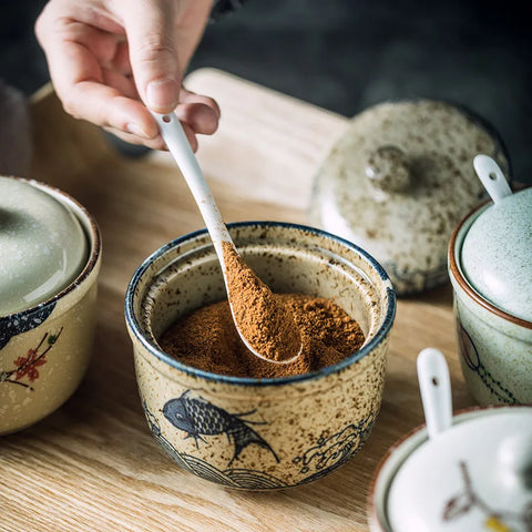 Spice dishes on table with person using a spoon to scoop out spices